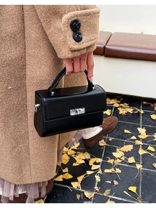 Détail d'un sac à main noir en cuir avec fermoir rotatif argenté sur fond automnal