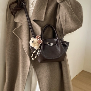 Detail of coffee brown leather bucket bag with silver turn-lock and cute plush bear charm