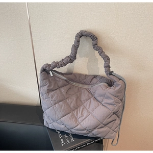 Detail of grey quilted tote bag with scrunchie handle and checkered cord on leather sofa