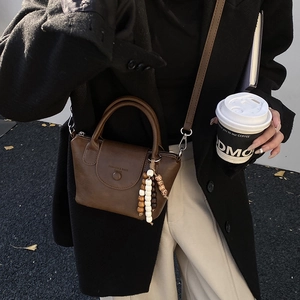 Detail of a dark brown mini leather handbag featuring a wooden bead charm and shoulder strap