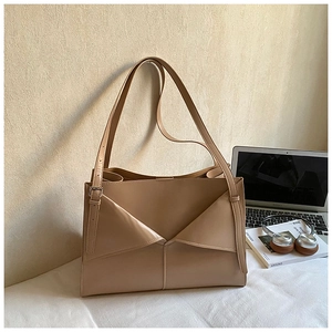Dettaglio della borsa tote in ecopelle beige con design geometrico piegato sulla scrivania