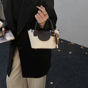 Close-up of cream and brown mini tote bag with wooden bead charm in a street style view