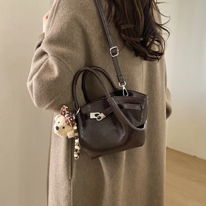 Deep brown glossy bucket bag shown on model with fuzzy bear charm and long shoulder strap