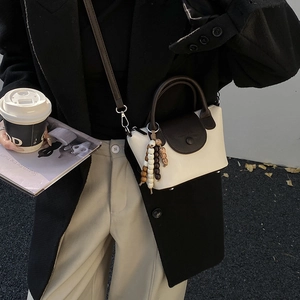 Outdoor street view of a minimalist beige leather crossbody bag with dark brown wood bead accents