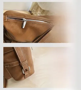 Detail view of smooth metal zipper and white contrast stitching on brown leather bag