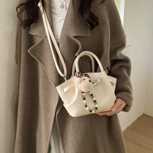 Close-up of beige bucket bag featuring a plush bear charm and beaded chain on a wool coat