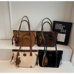 Four textured suede tote bags in various colors with cute bear charms on marble steps