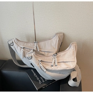 Detail of two beige crescent crossbody bags with woven zippers on nylon fabric