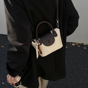 Chic contrast-color crossbody bag with white body, dark flap, and beaded strap detail
