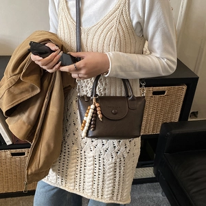 Deep brown leather crossbody bag with wooden bead charm detail shown on a model