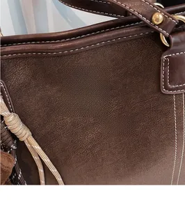 Detail of dark brown tote bag with white stitching and gold brand logo on pebble leather