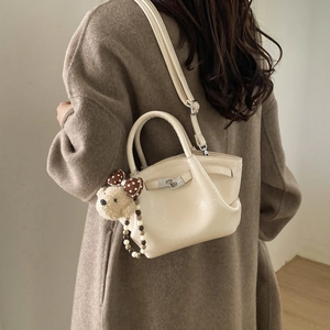 Detail of off-white leather bucket bag with silver turn-lock and cute teddy bear charm