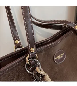 Close-up of brown tote bag showing durable golden hardware and contrast stitching details