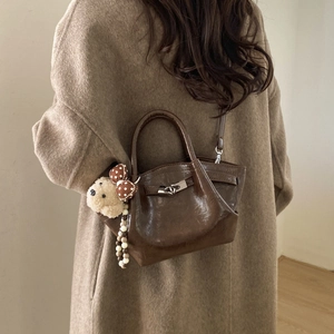 Detail of caramel bucket bag with silver clasp, plush bear charm and glossy finish