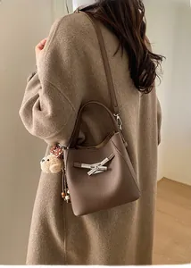 Detail of brown litchi pattern bucket bag featuring a silver metal cross lock and bear charm