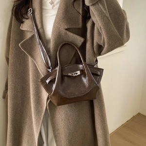 Detail of dark brown polished leather bucket bag worn with a stylish khaki wool coat