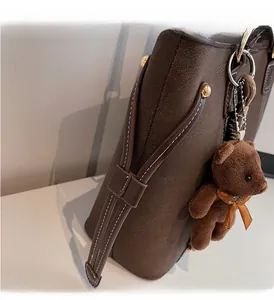 Detail of dark brown pebbled leather tote with white stitching and bear plush charm