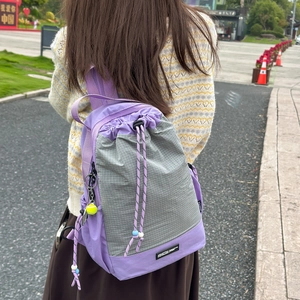 Dettaglio zaino in nylon lavanda con chiusura a coulisse, pannello a scacchi e charm tennis