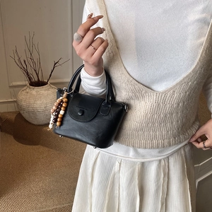 Detail of a minimalist black leather handbag with a stylish wooden bead tassel accent