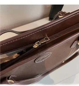 Close-up of smooth golden metal zipper and white stitching on dark brown leather tote bag