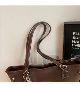 Detail of reinforced leather handles with white contrast stitching on a dark brown tote bag