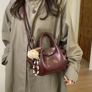 Detail of dark red bucket bag with polished finish, metal lock, and plush dog charm