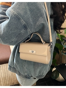 Sac bandoulière beige en similicuir avec fermoir rotatif et pieds en métal porté par un mannequin