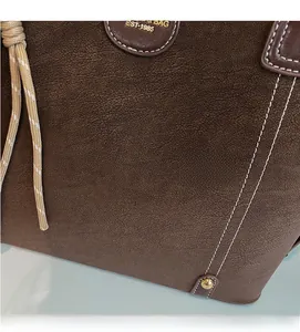 Detail of dark brown matte leather tote with white stitching and gold metal rivet
