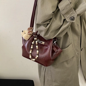 Detail of dark burgundy bucket bag with silver lock, plush bear and beaded charm accents