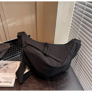Detail of a black crescent crossbody bag with braided rope zippers on an office desk