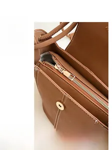 Detail view of brown leather bucket bag with gold zipper and magnetic closure