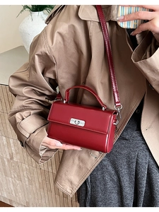 Detail of a dark red retro square handbag featuring a silver metal twist lock and leather strap