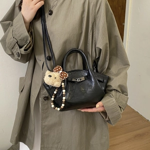 Detail of black pleated patent leather bucket bag with silver lock and cute bear charm