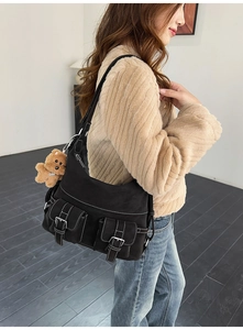 Detail of black canvas tote bag with white stitching and plush bear charm on side