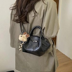 Detail of a black pleated bucket bag with a cute teddy bear charm on a shoulder strap