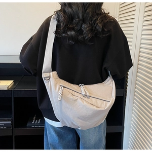 Rear view of a beige nylon crossbody dumpling bag with wide strap on a model