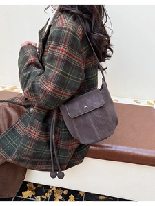 Detail of a dark brown bucket bag with white contrast stitching and decorative round beads