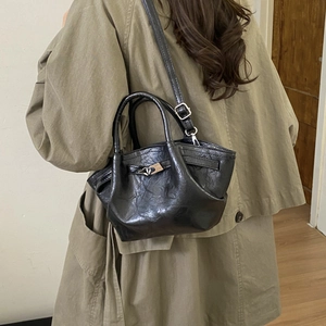 Detail of black wrinkled leather bucket bag shown on model with khaki trench coat