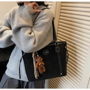 Detail of black tote bag with white stitching and plush bear charm on model shoulder