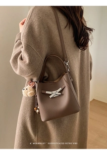 Detail of a brown lychee pattern bucket bag with silver knot buckle and teddy bear charm