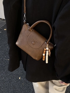 Retro brown soft leather crossbody bag with beaded charm shown in an outdoor street scene