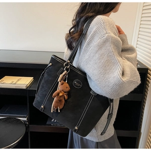 Close-up of black matte tote bag with contrast white stitching and plush bear charm