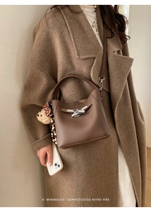 Detail of dark brown lychee leather bucket bag with silver lock and bear pendant
