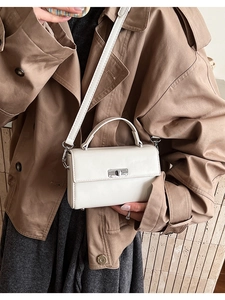 Détail du sac à bandoulière en cuir blanc avec fermoir argenté porté avec un trench-coat