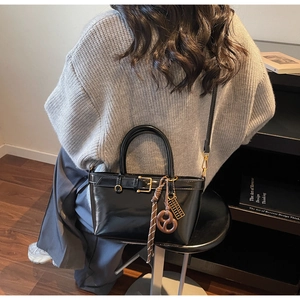 Detail of a black bucket bag featuring decorative belts and charms on a seated model