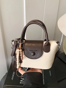 Minimalist cream and brown leather handbag with wooden beads shown on decorative books