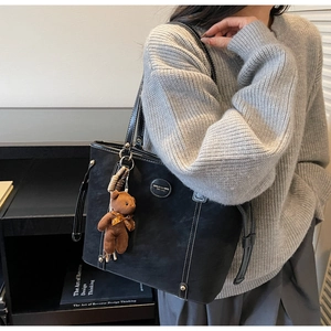 Detail of black suede tote bag featuring contrast stitching and a brown teddy bear charm