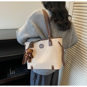 Detailed view of cream tote bag with brown trim and plush bear charm on model