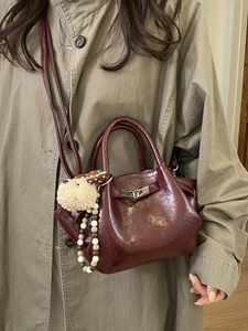 Burgundy pleated bucket bag with heart buckle and plush dog charm on khaki trench coat