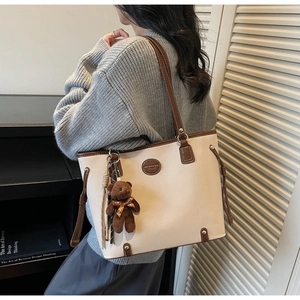 Detail of a beige tote bag with brown leather trim and a cute plush bear charm